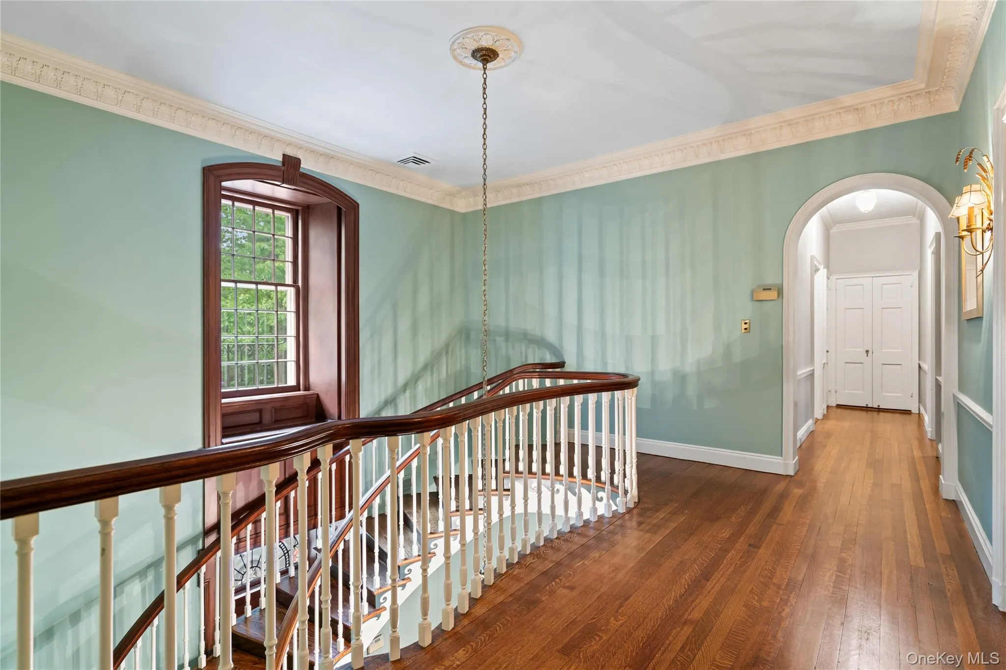 Stairway featuring hardwood / wood-style flooring, ornamental molding, and arched walkways Stairway featuring hardwood / wood-style flooring, ornamental molding, and arched walkways