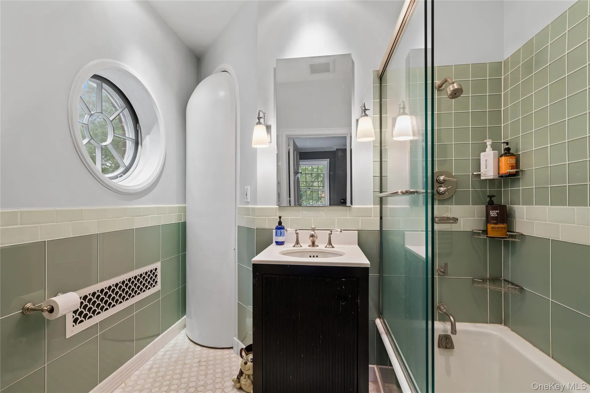 Full bathroom featuring bath / shower combo with glass door, vanity, tile walls, and wainscoting Full bathroom featuring bath / shower combo with glass door, vanity, tile walls, and wainscoting