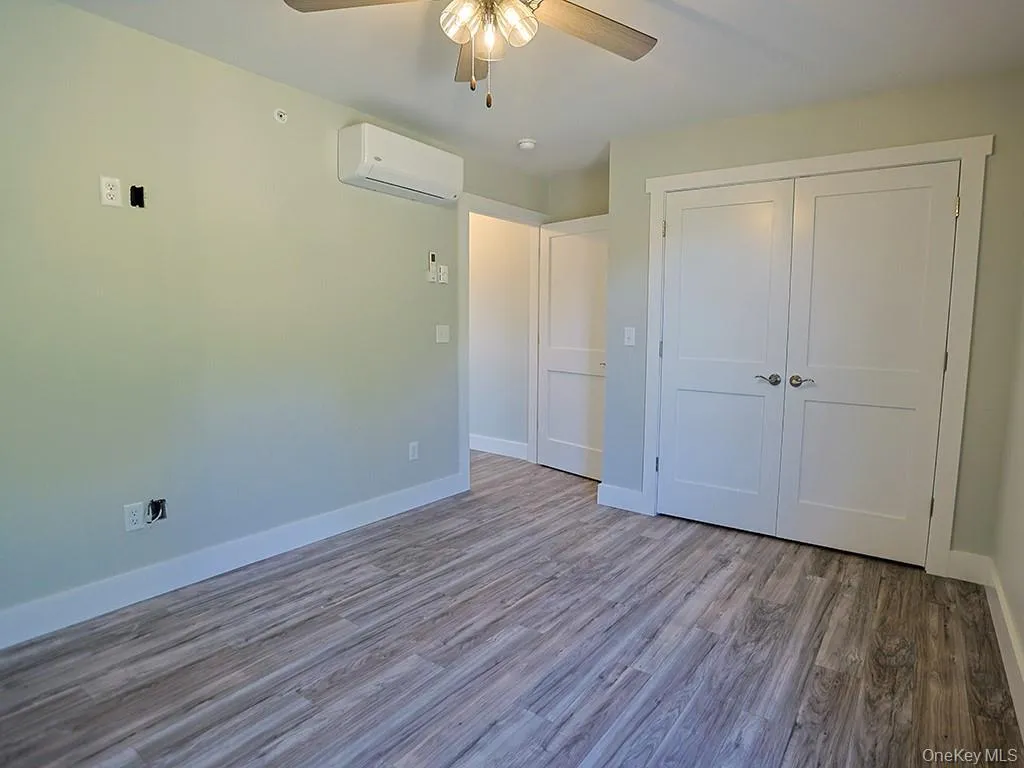 Unfurnished bedroom with wood finished floors, a ceiling fan, a wall mounted air conditioner, and a closet Unfurnished bedroom with wood finished floors, a ceiling fan, a wall mounted air conditioner, and a closet
