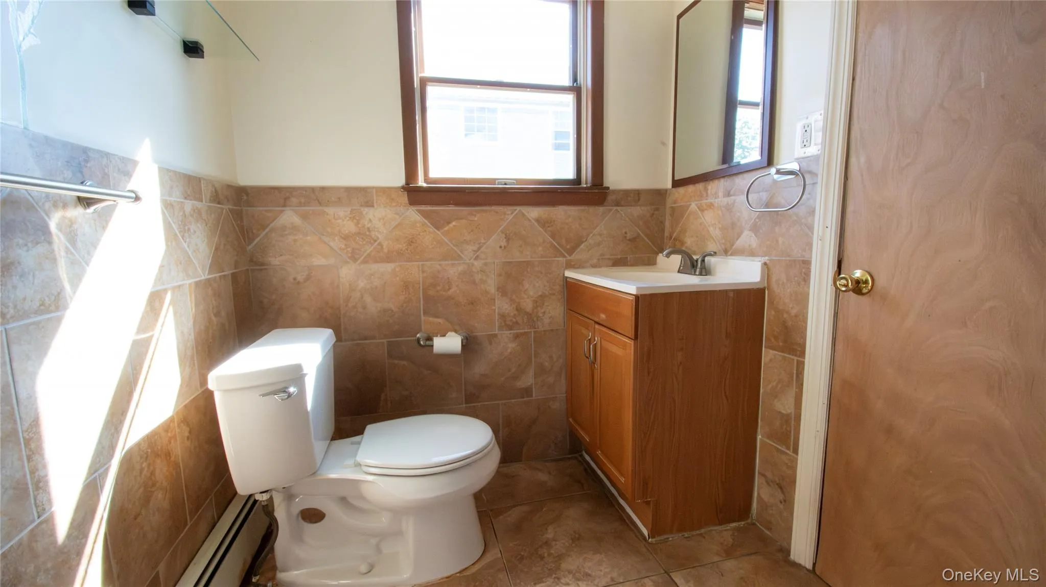 Bathroom with baseboard heating, vanity, light tile patterned flooring, and tile walls Bathroom with baseboard heating, vanity, light tile patterned flooring, and tile walls