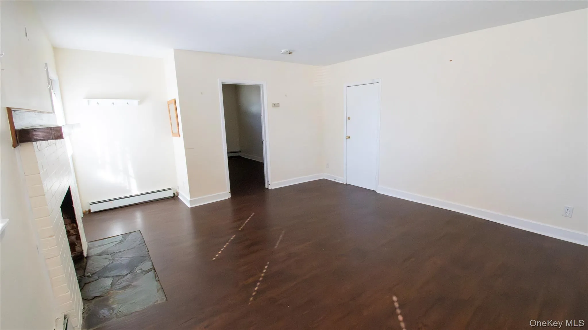 Empty room with dark wood-style floors, a baseboard radiator, and a fireplace Empty room with dark wood-style floors, a baseboard radiator, and a fireplace