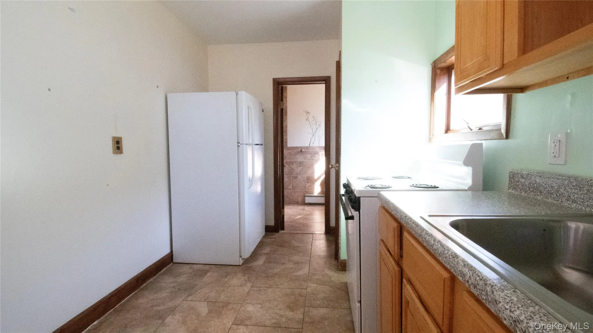 Kitchen featuring white appliances, brown cabinetry, light countertops, and a baseboard radiator Kitchen featuring white appliances, brown cabinetry, light countertops, and a baseboard radiator