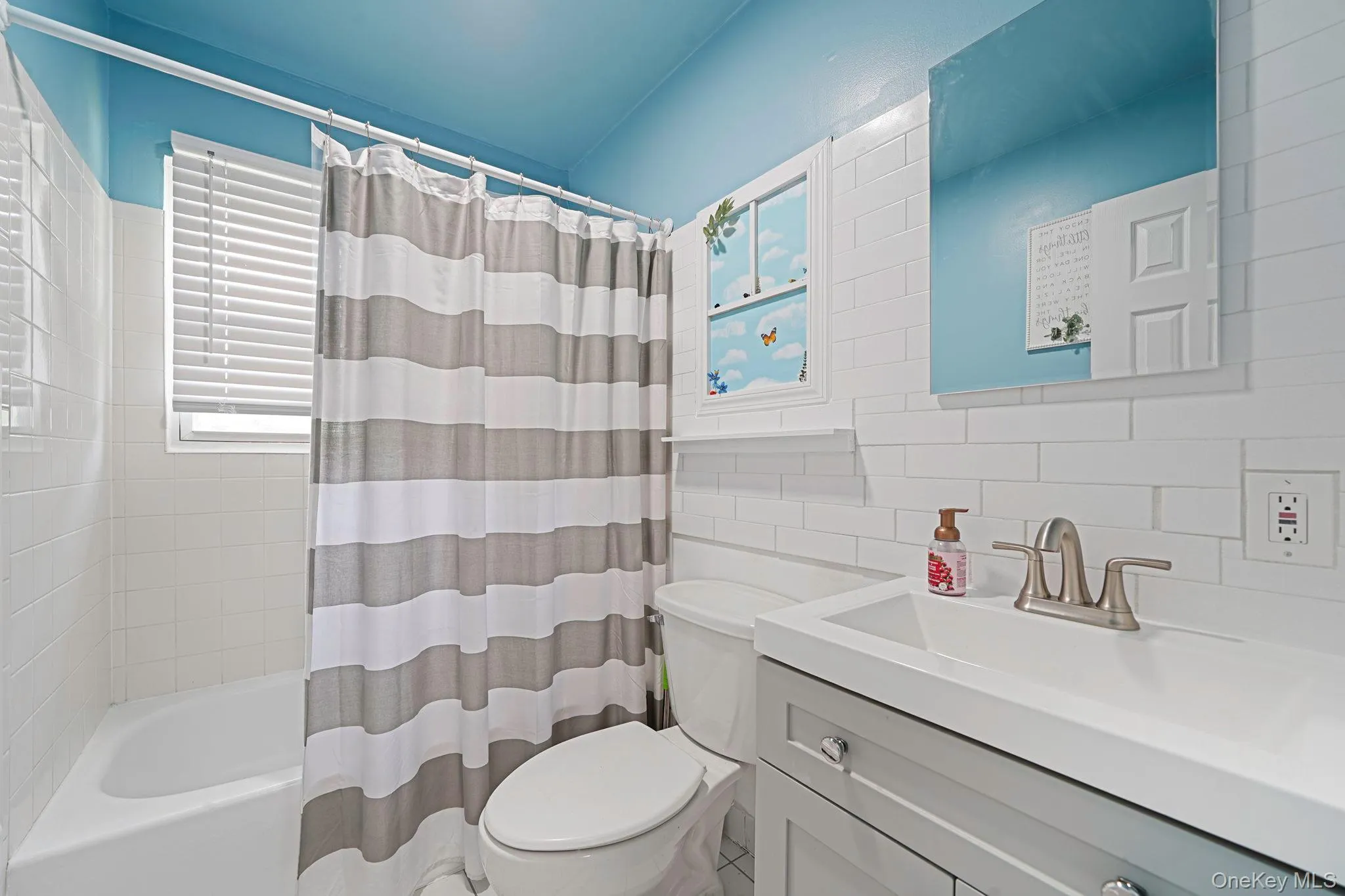 Bathroom featuring shower / tub combo with curtain, tile walls, vanity, and backsplash Bathroom featuring shower / tub combo with curtain, tile walls, vanity, and backsplash