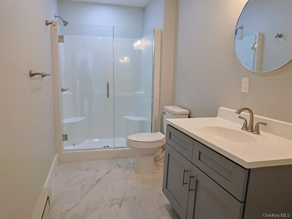 Full bathroom featuring a shower stall, vanity, light marble finish flooring, and a baseboard heating unit Full bathroom featuring a shower stall, vanity, light marble finish flooring, and a baseboard heating unit