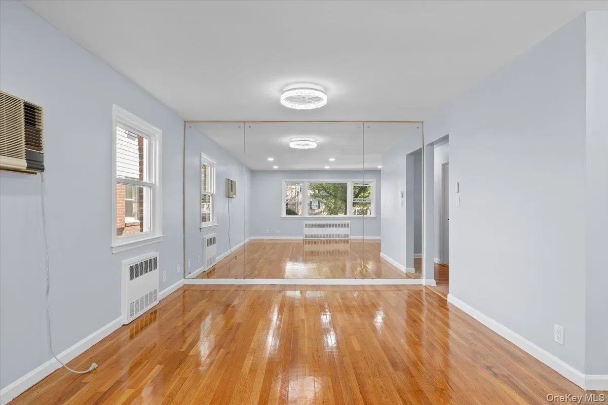 Unfurnished room with wood-type flooring, radiator heating unit, and an AC wall unit Unfurnished room with wood-type flooring, radiator heating unit, and an AC wall unit