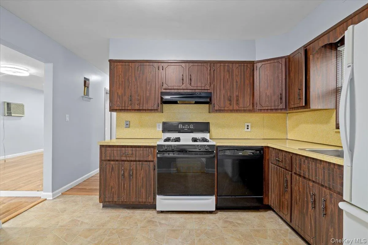Kitchen featuring white appliances, decorative backsplash, light countertops, and under cabinet range hood Kitchen featuring white appliances, decorative backsplash, light countertops, and under cabinet range hood