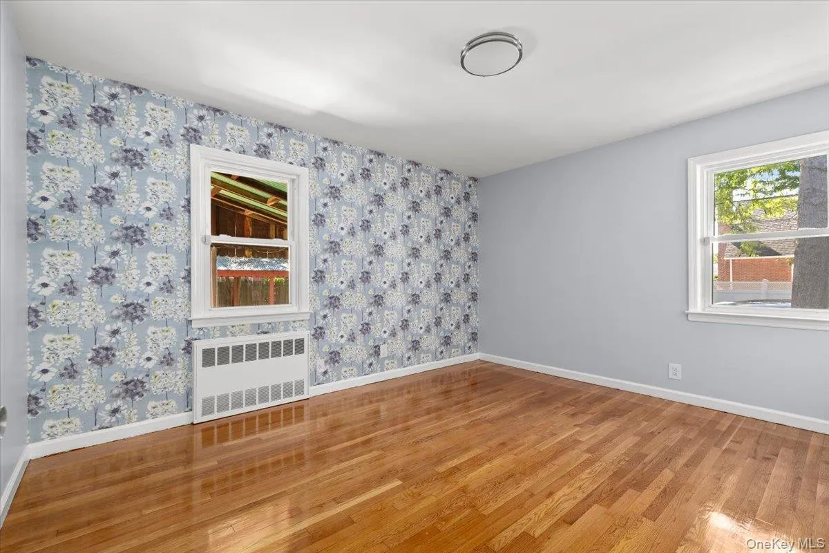 Unfurnished room featuring radiator, light wood-type flooring, and wallpapered walls Unfurnished room featuring radiator, light wood-type flooring, and wallpapered walls