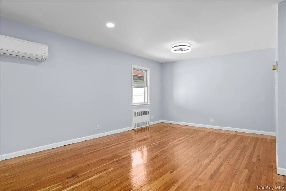 Empty room with light wood finished floors, an AC wall unit, radiator heating unit, and recessed lighting Empty room with light wood finished floors, an AC wall unit, radiator heating unit, and recessed lighting