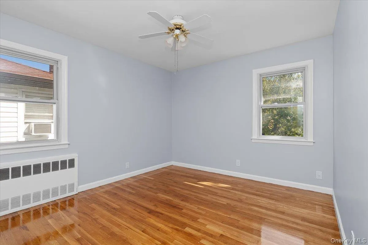 Empty room with radiator, light wood-type flooring, and a ceiling fan Empty room with radiator, light wood-type flooring, and a ceiling fan