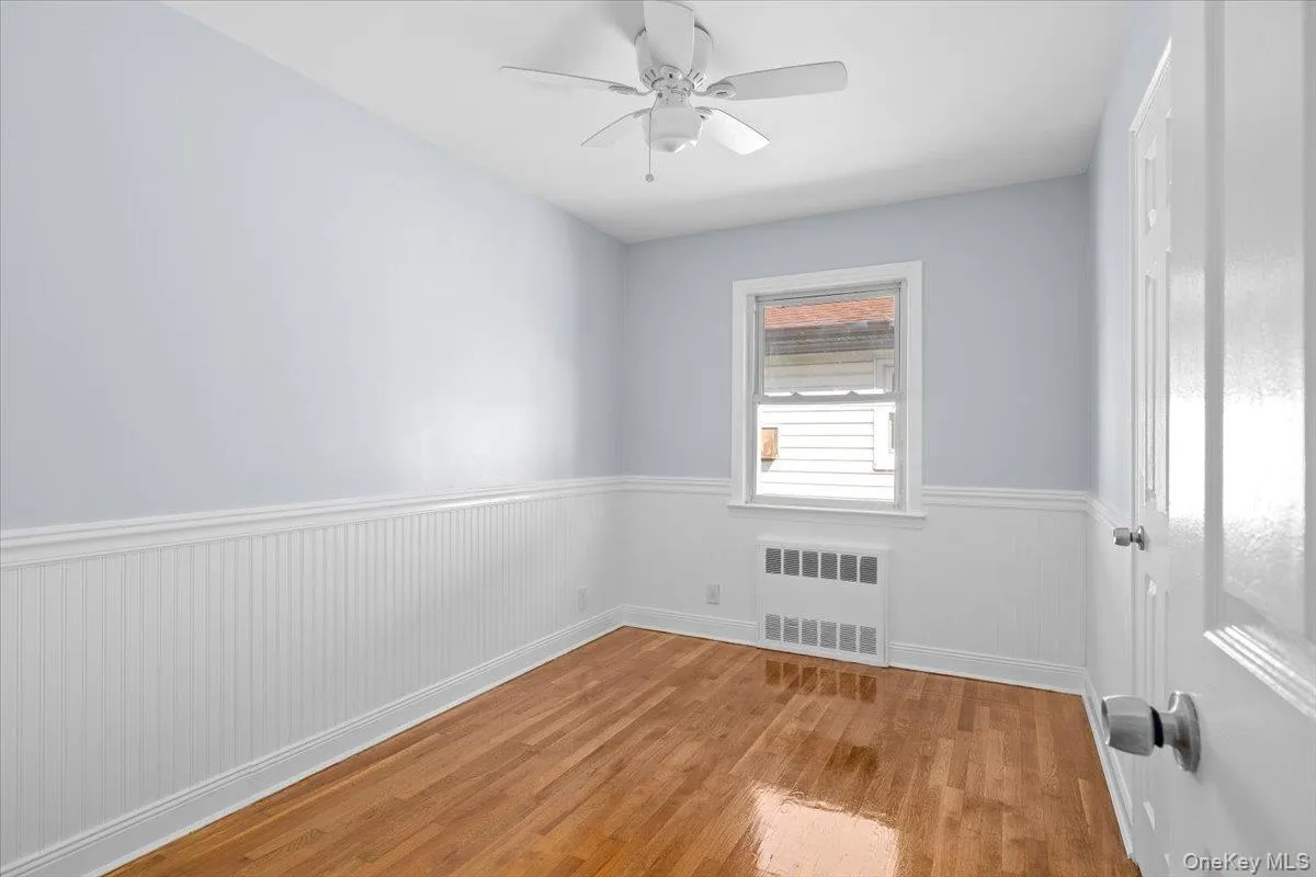 Unfurnished room with wainscoting, light wood finished floors, radiator heating unit, and a ceiling fan Unfurnished room with wainscoting, light wood finished floors, radiator heating unit, and a ceiling fan