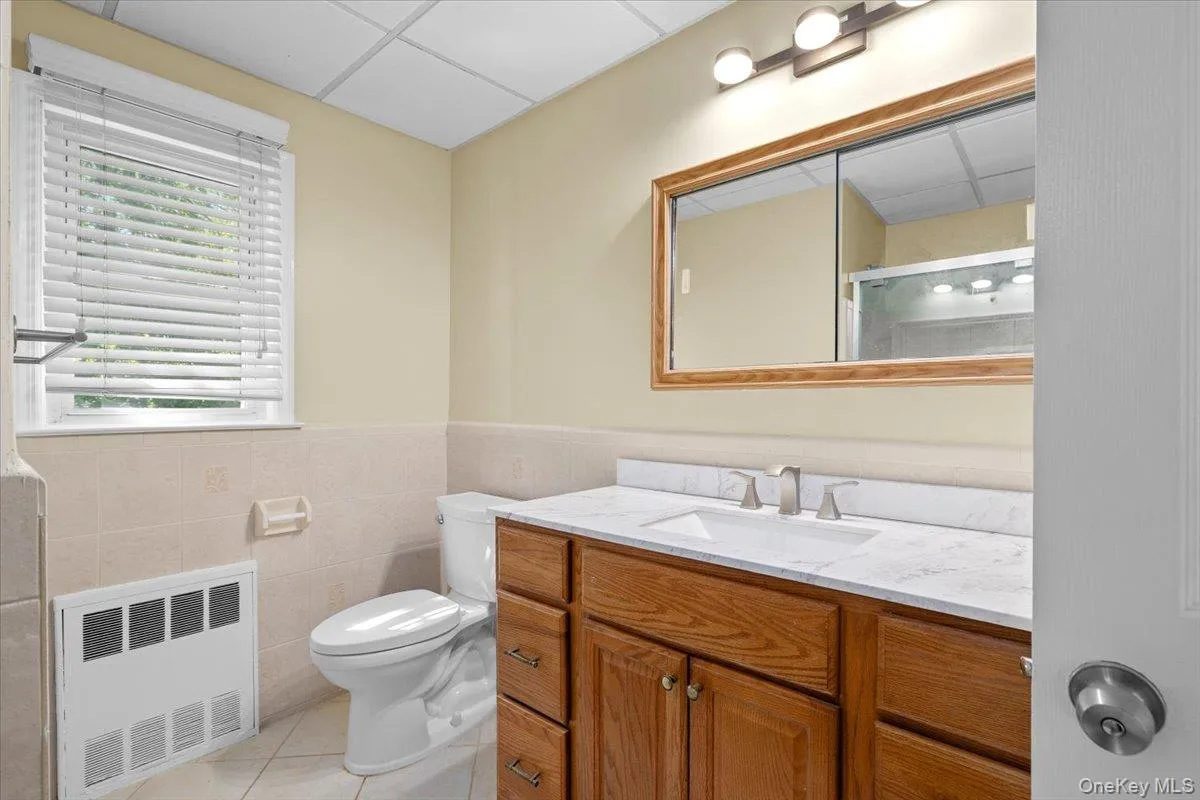 Full bath featuring light tile patterned floors, vanity, a shower stall, a drop ceiling, and tile walls Full bath featuring light tile patterned floors, vanity, a shower stall, a drop ceiling, and tile walls