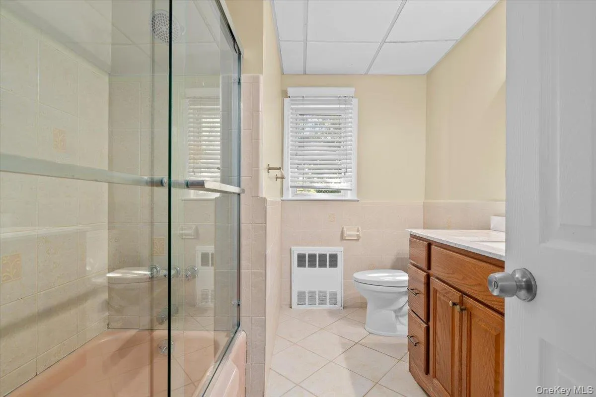 Bathroom with vanity, light tile patterned floors, enclosed tub / shower combo, tile walls, and a drop ceiling Bathroom with vanity, light tile patterned floors, enclosed tub / shower combo, tile walls, and a drop ceiling