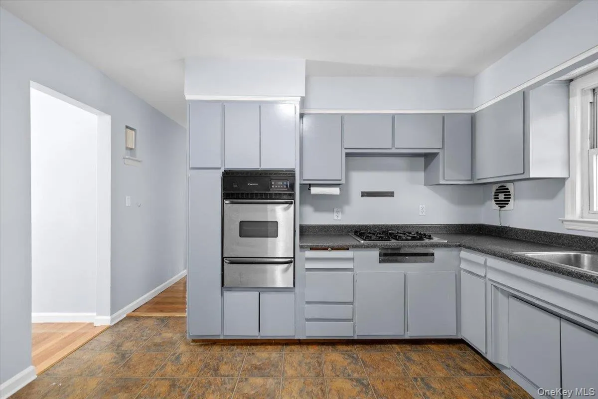 Kitchen with dark countertops, stainless steel oven, a warming drawer, gray cabinets, and stone finish flooring Kitchen with dark countertops, stainless steel oven, a warming drawer, gray cabinets, and stone finish flooring