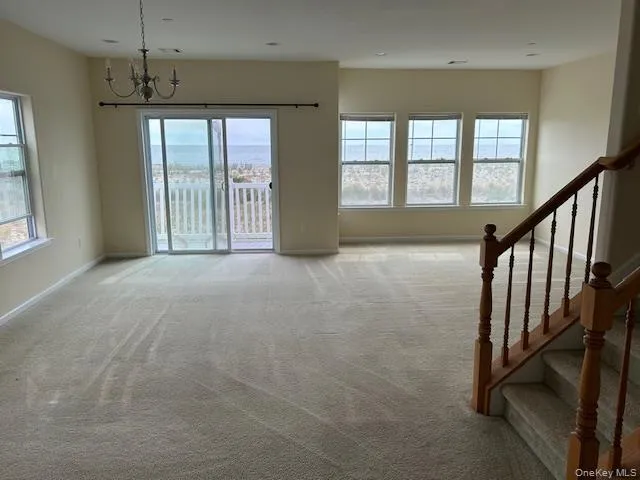 Unfurnished living room featuring plenty of natural light, a chandelier, carpet, and stairway Unfurnished living room featuring plenty of natural light, a chandelier, carpet, and stairway