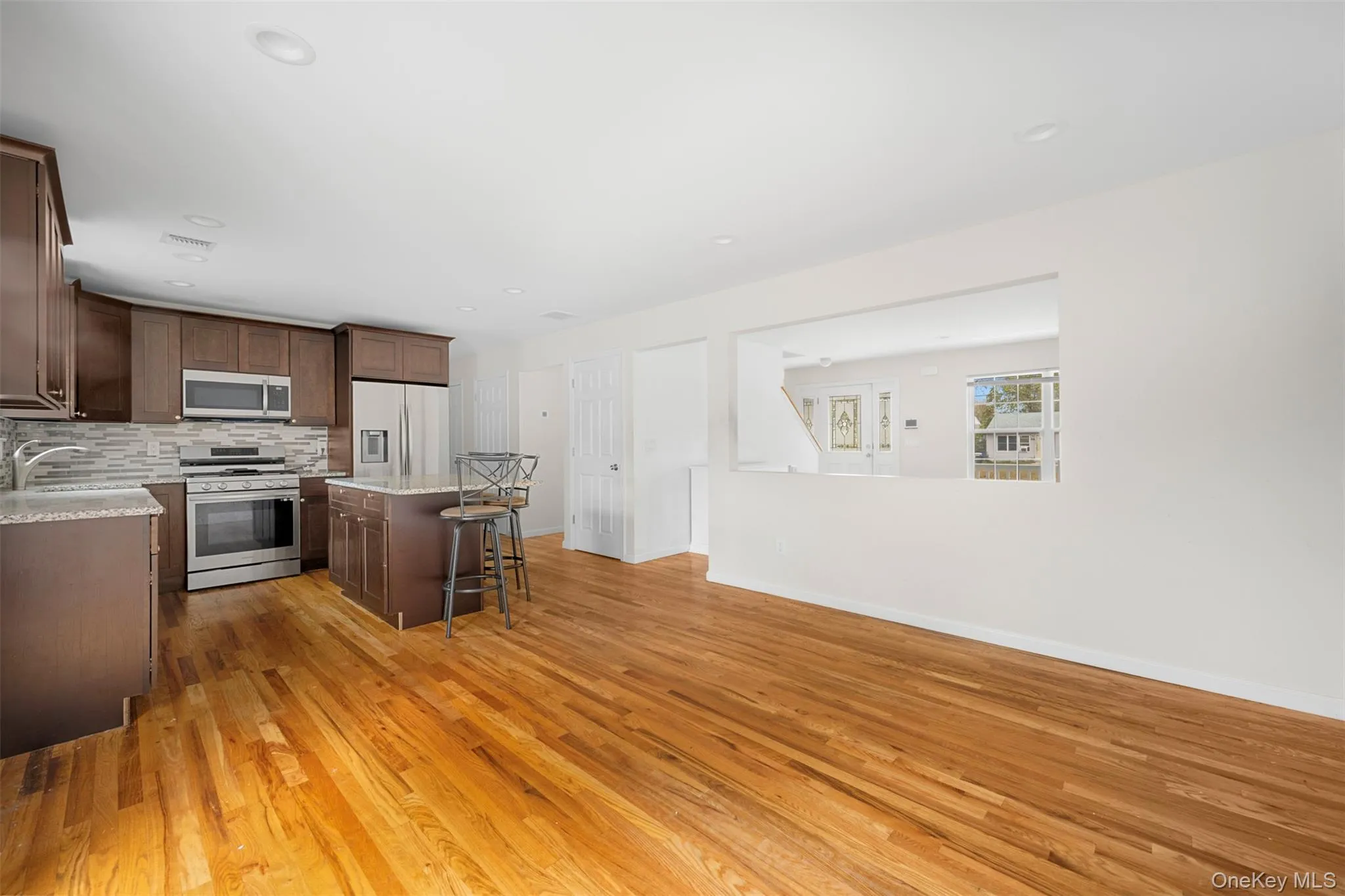 Kitchen featuring stainless steel appliances, a breakfast bar, decorative backsplash, light wood-style flooring, and a kitchen island Kitchen featuring stainless steel appliances, a breakfast bar, decorative backsplash, light wood-style flooring, and a kitchen island