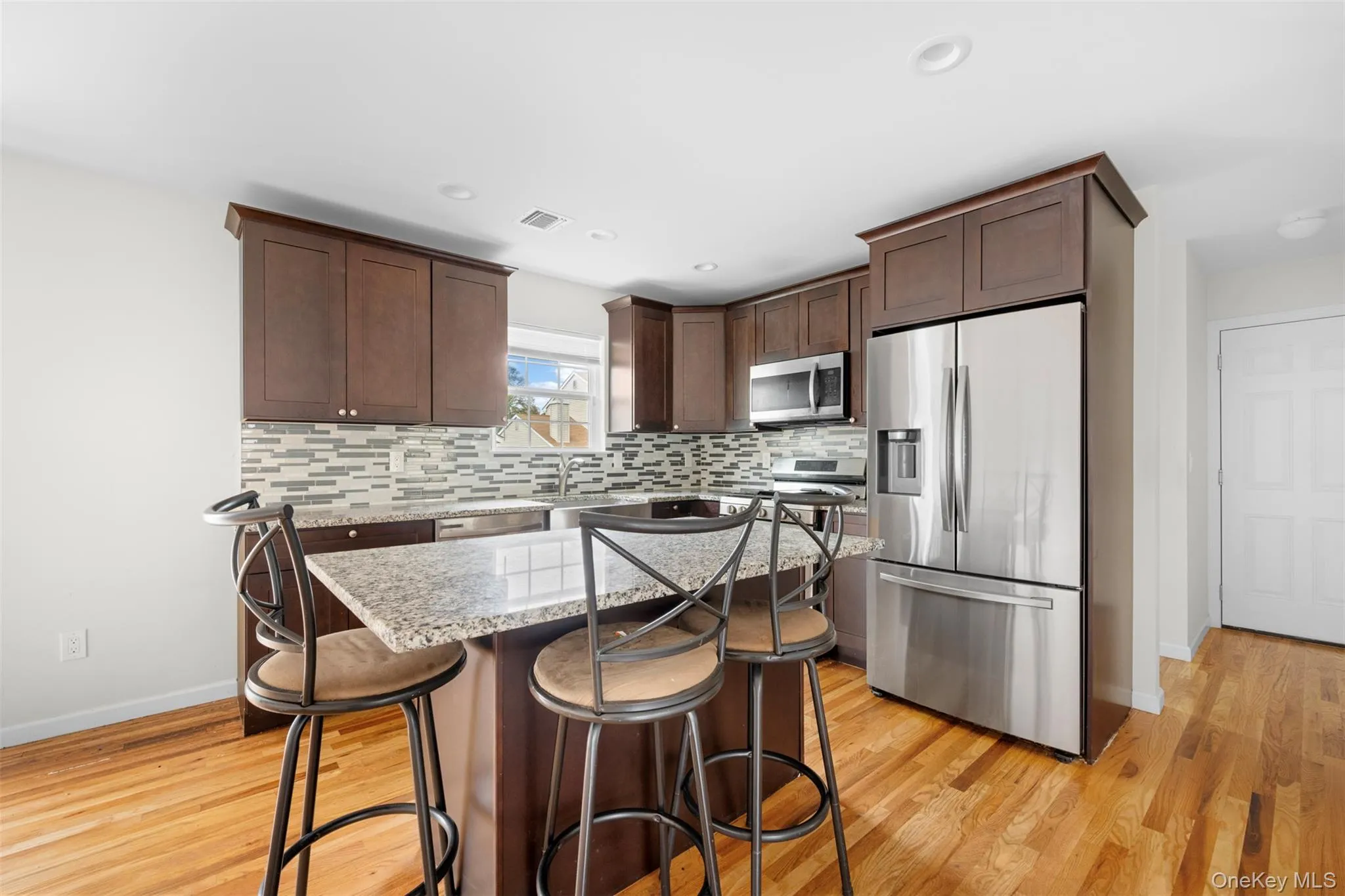 Kitchen with dark brown cabinets, a kitchen bar, light stone countertops, appliances with stainless steel finishes, and tasteful backsplash Kitchen with dark brown cabinets, a kitchen bar, light stone countertops, appliances with stainless steel finishes, and tasteful backsplash
