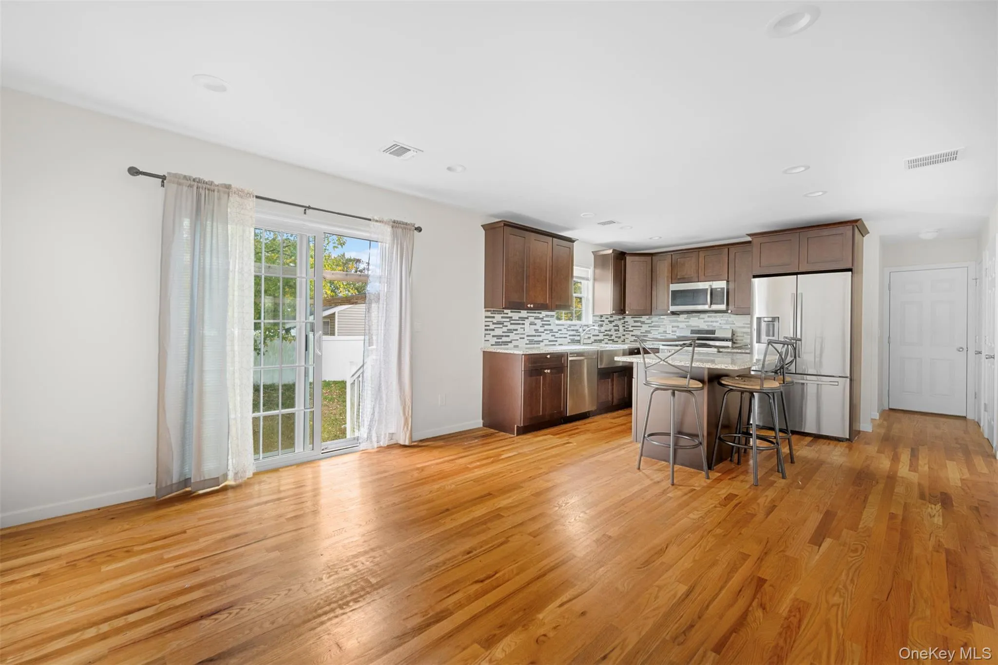 Kitchen featuring a breakfast bar, appliances with stainless steel finishes, decorative backsplash, a kitchen island, and light wood-style floors Kitchen featuring a breakfast bar, appliances with stainless steel finishes, decorative backsplash, a kitchen island, and light wood-style floors