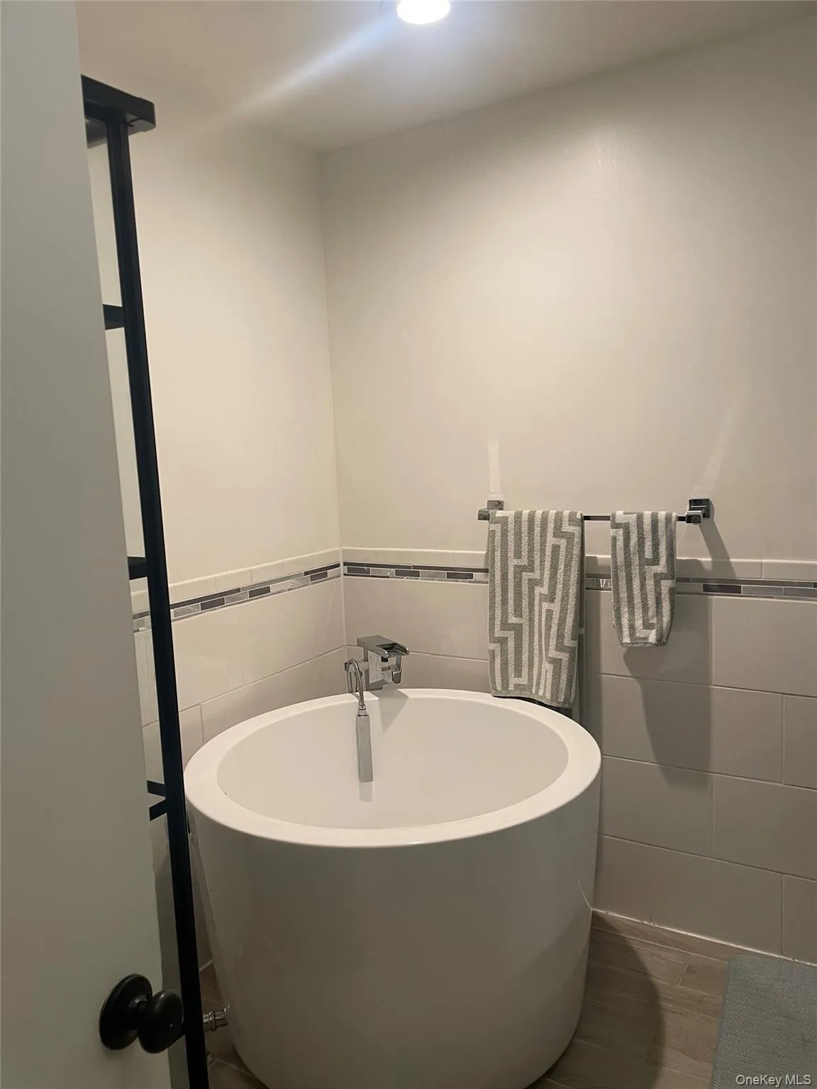 Full bath with a freestanding bath, tile walls, wainscoting, and wood finished floors Full bath with a freestanding bath, tile walls, wainscoting, and wood finished floors