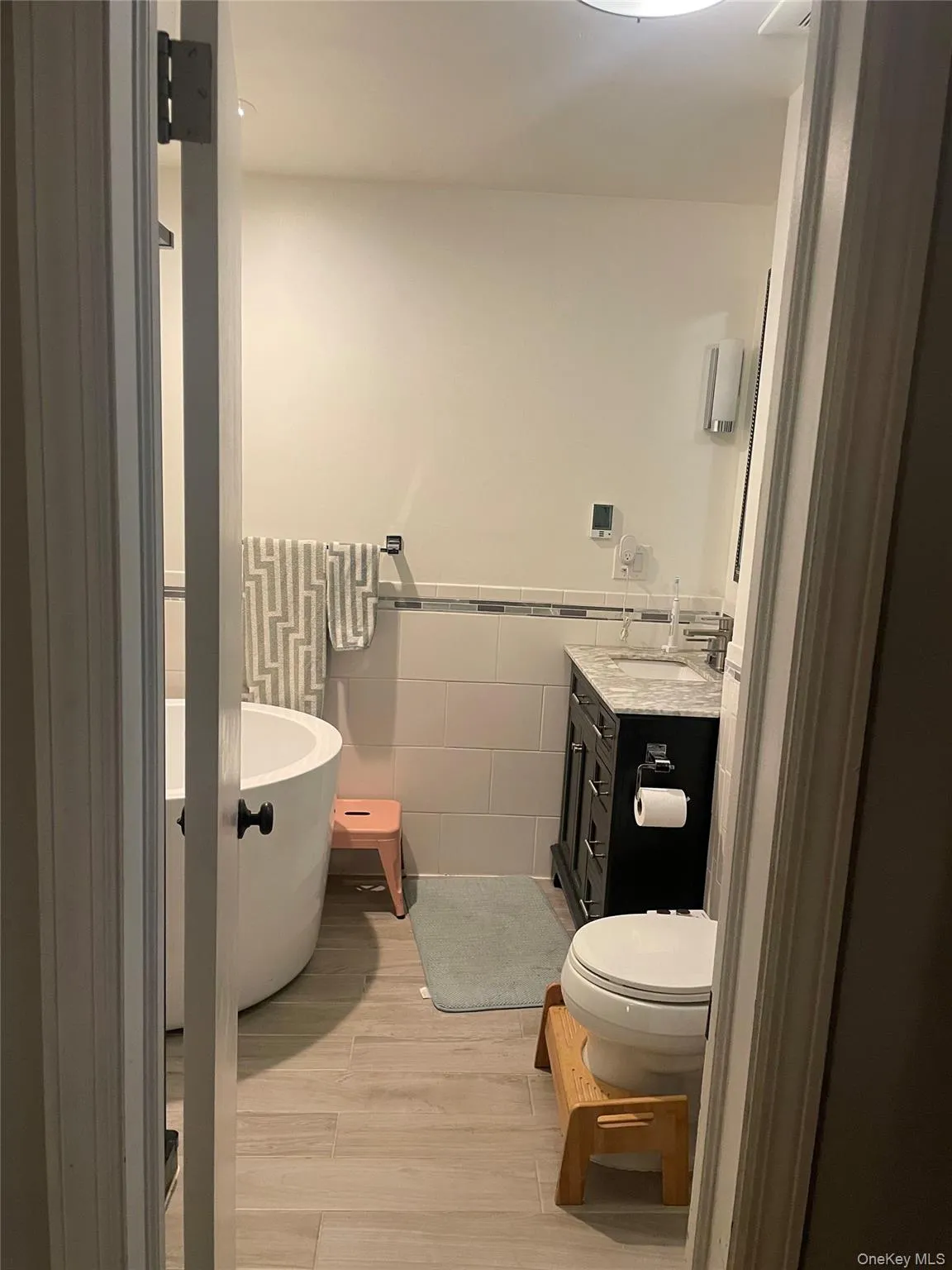 Full bath with tile walls, vanity, a freestanding bath, a wainscoted wall, and light wood-style floors Full bath with tile walls, vanity, a freestanding bath, a wainscoted wall, and light wood-style floors