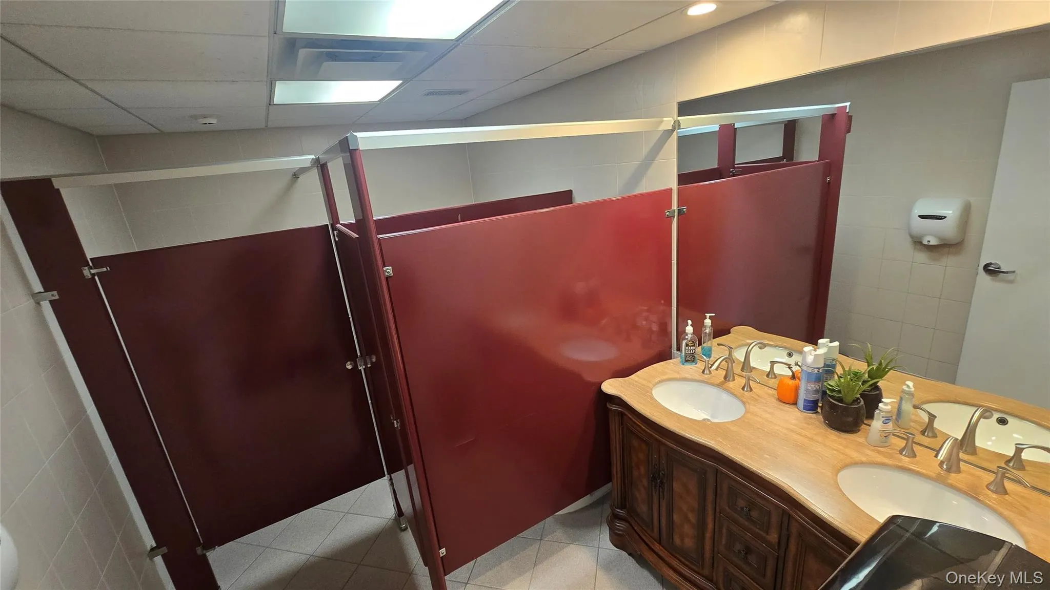 Full bathroom featuring double vanity, a shower stall, light tile patterned floors, tile walls, and a drop ceiling Full bathroom featuring double vanity, a shower stall, light tile patterned floors, tile walls, and a drop ceiling