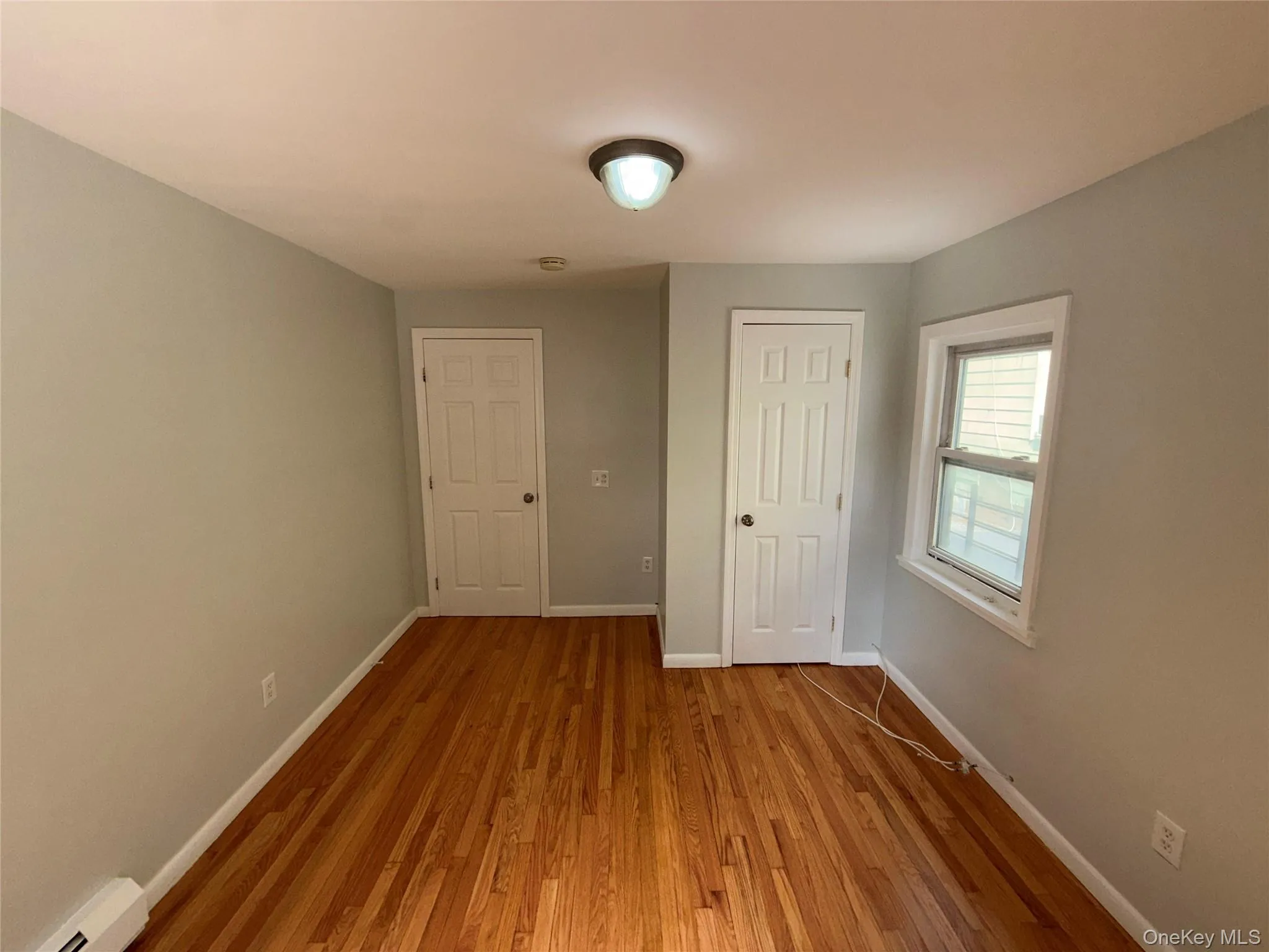 Unfurnished bedroom featuring hardwood / wood-style flooring, a baseboard radiator, and a closet Unfurnished bedroom featuring hardwood / wood-style flooring, a baseboard radiator, and a closet