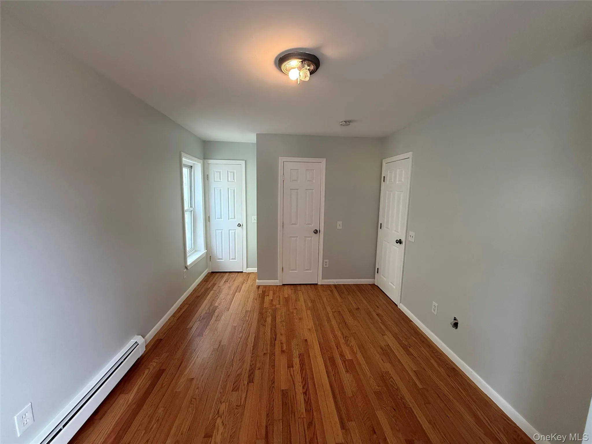 Unfurnished room with a baseboard heating unit and wood finished floors Unfurnished room with a baseboard heating unit and wood finished floors