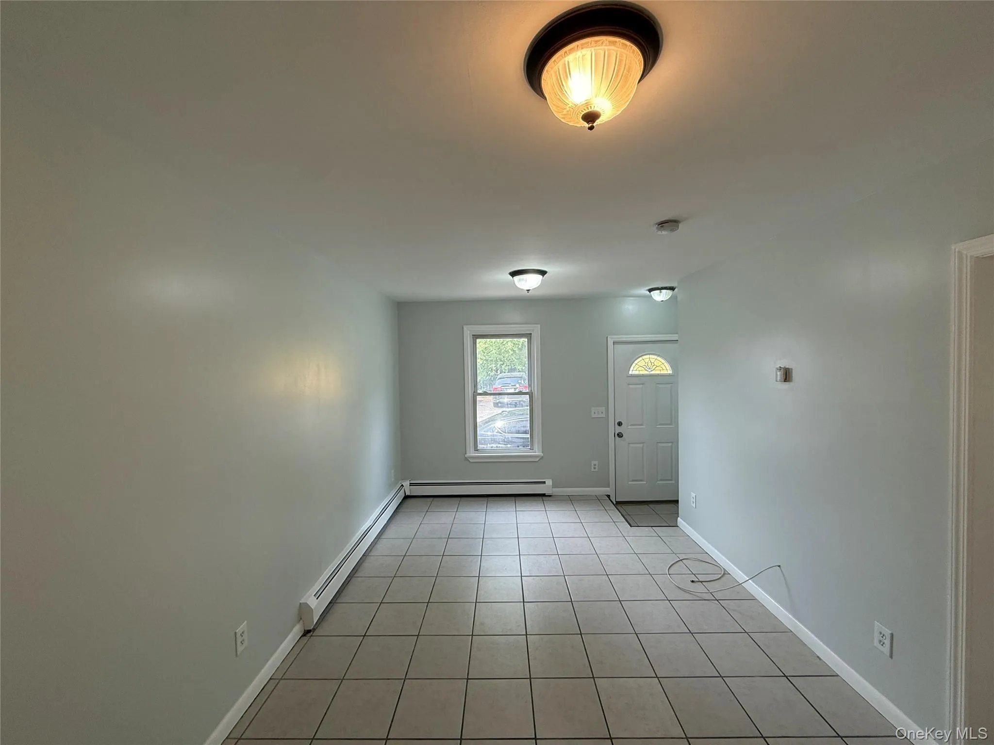 Empty room with light tile patterned flooring and a baseboard heating unit Empty room with light tile patterned flooring and a baseboard heating unit