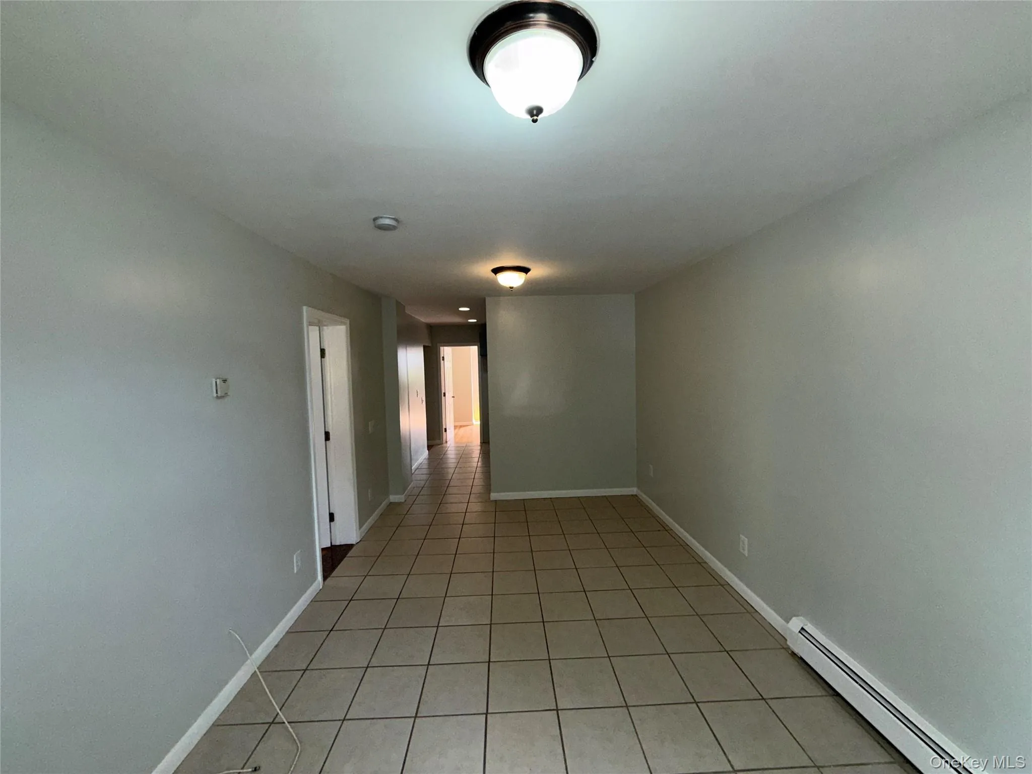 Empty room with baseboard heating and light tile patterned floors Empty room with baseboard heating and light tile patterned floors