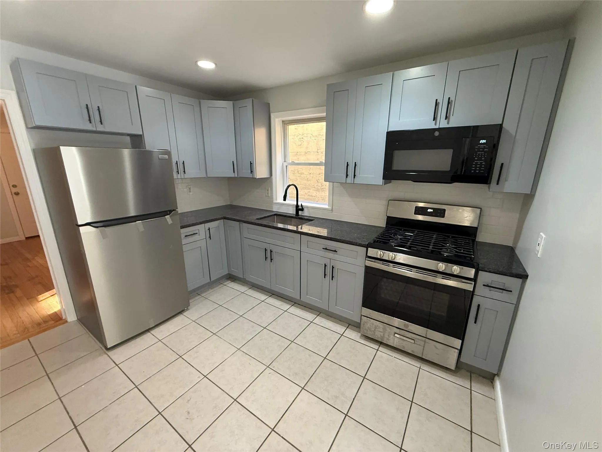 Kitchen with appliances with stainless steel finishes, gray cabinetry, dark stone counters, light tile patterned flooring, and recessed lighting Kitchen with appliances with stainless steel finishes, gray cabinetry, dark stone counters, light tile patterned flooring, and recessed lighting