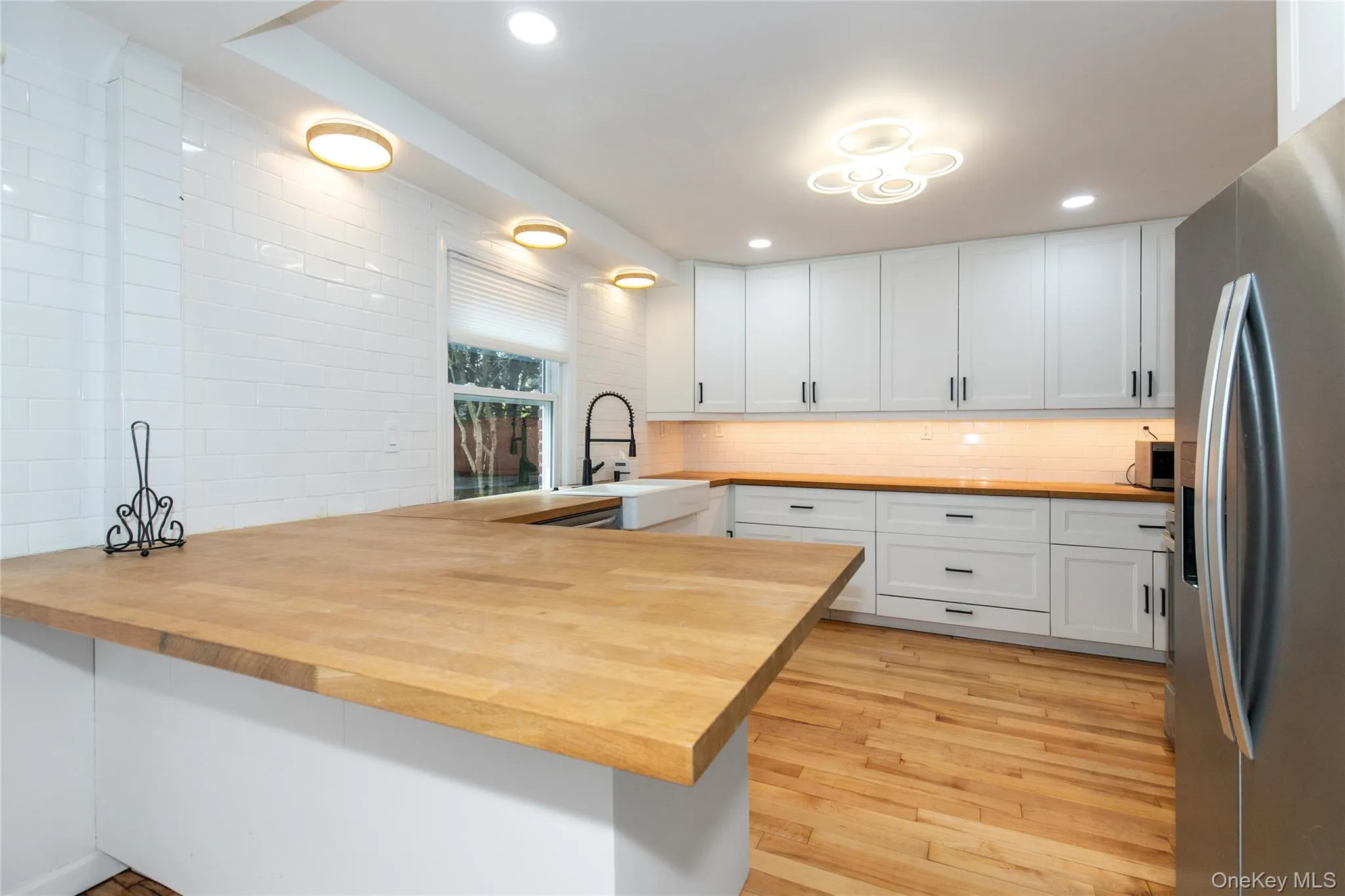Kitchen with a peninsula, stainless steel fridge, white cabinets, butcher block counters, and light wood-type flooring Kitchen with a peninsula, stainless steel fridge, white cabinets, butcher block counters, and light wood-type flooring
