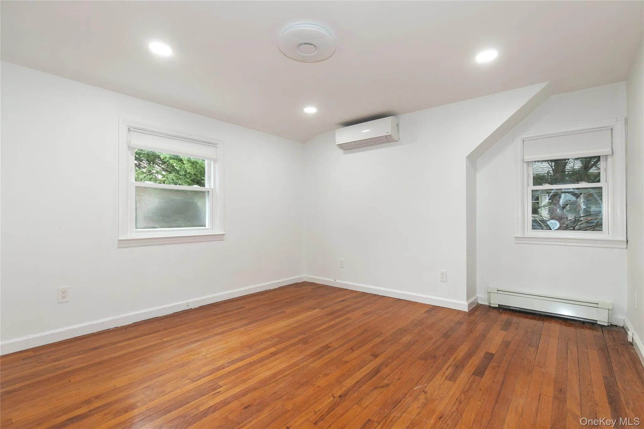 Empty room featuring a baseboard heating unit, dark wood-type flooring, recessed lighting, and a wall mounted air conditioner Empty room featuring a baseboard heating unit, dark wood-type flooring, recessed lighting, and a wall mounted air conditioner