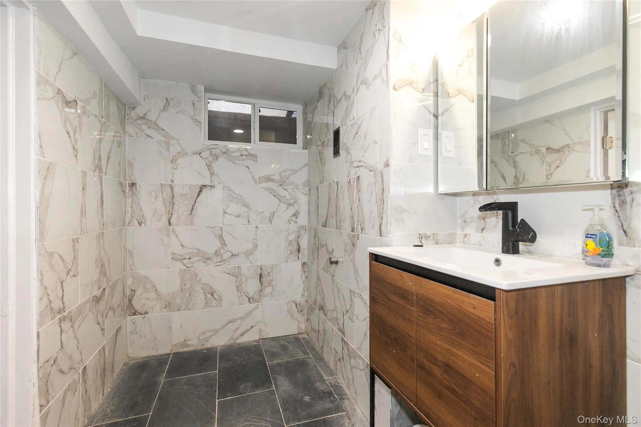 Bathroom with a marble finish shower, vanity, and tile walls Bathroom with a marble finish shower, vanity, and tile walls