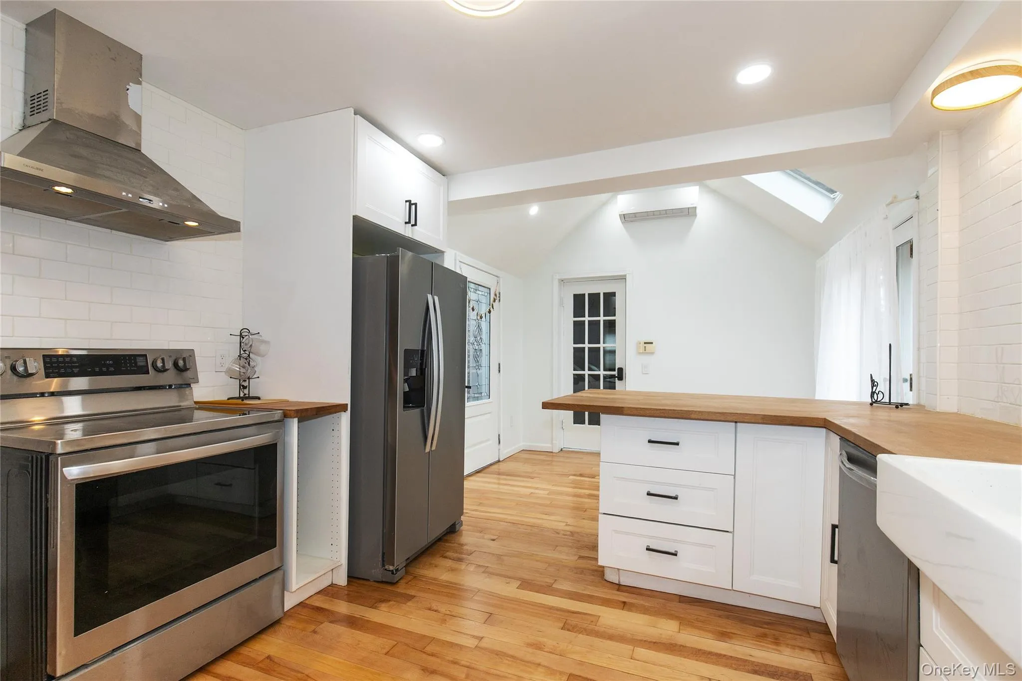 Kitchen featuring wood counters, appliances with stainless steel finishes, wall chimney range hood, white cabinets, and backsplash Kitchen featuring wood counters, appliances with stainless steel finishes, wall chimney range hood, white cabinets, and backsplash