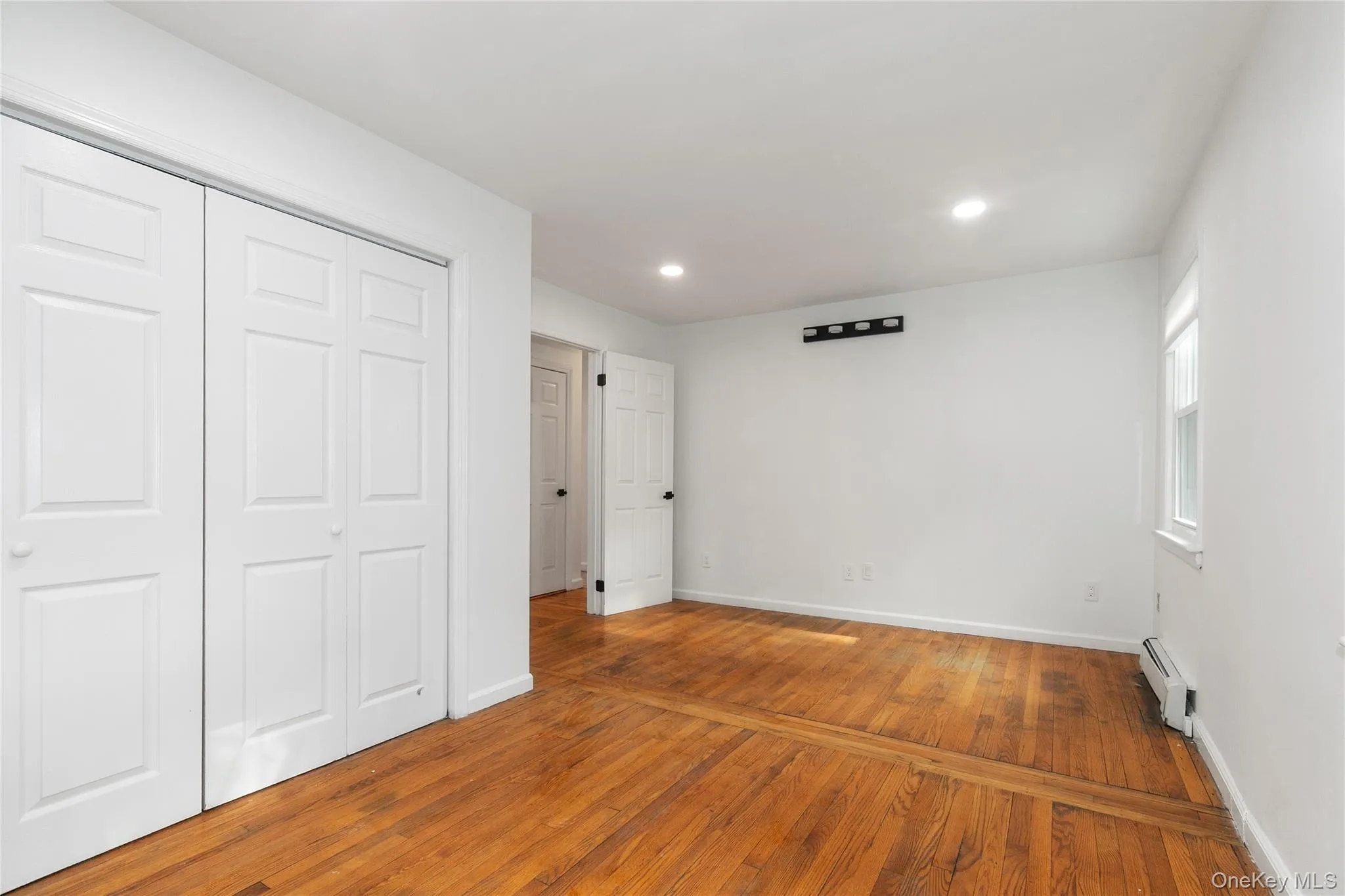 Unfurnished bedroom with hardwood / wood-style floors, a baseboard radiator, a closet, and recessed lighting Unfurnished bedroom with hardwood / wood-style floors, a baseboard radiator, a closet, and recessed lighting