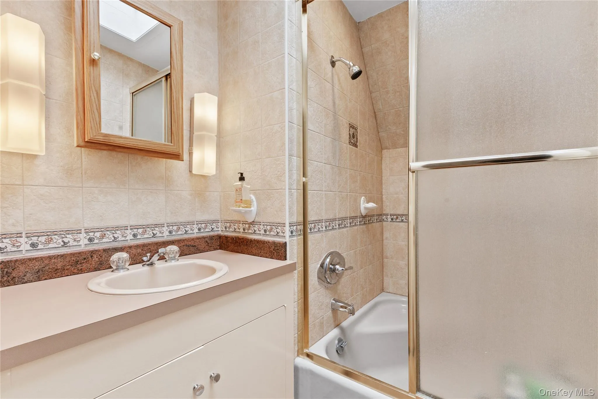 Full bathroom with bath / shower combo with glass door, vanity, tile walls, and backsplash Full bathroom with bath / shower combo with glass door, vanity, tile walls, and backsplash