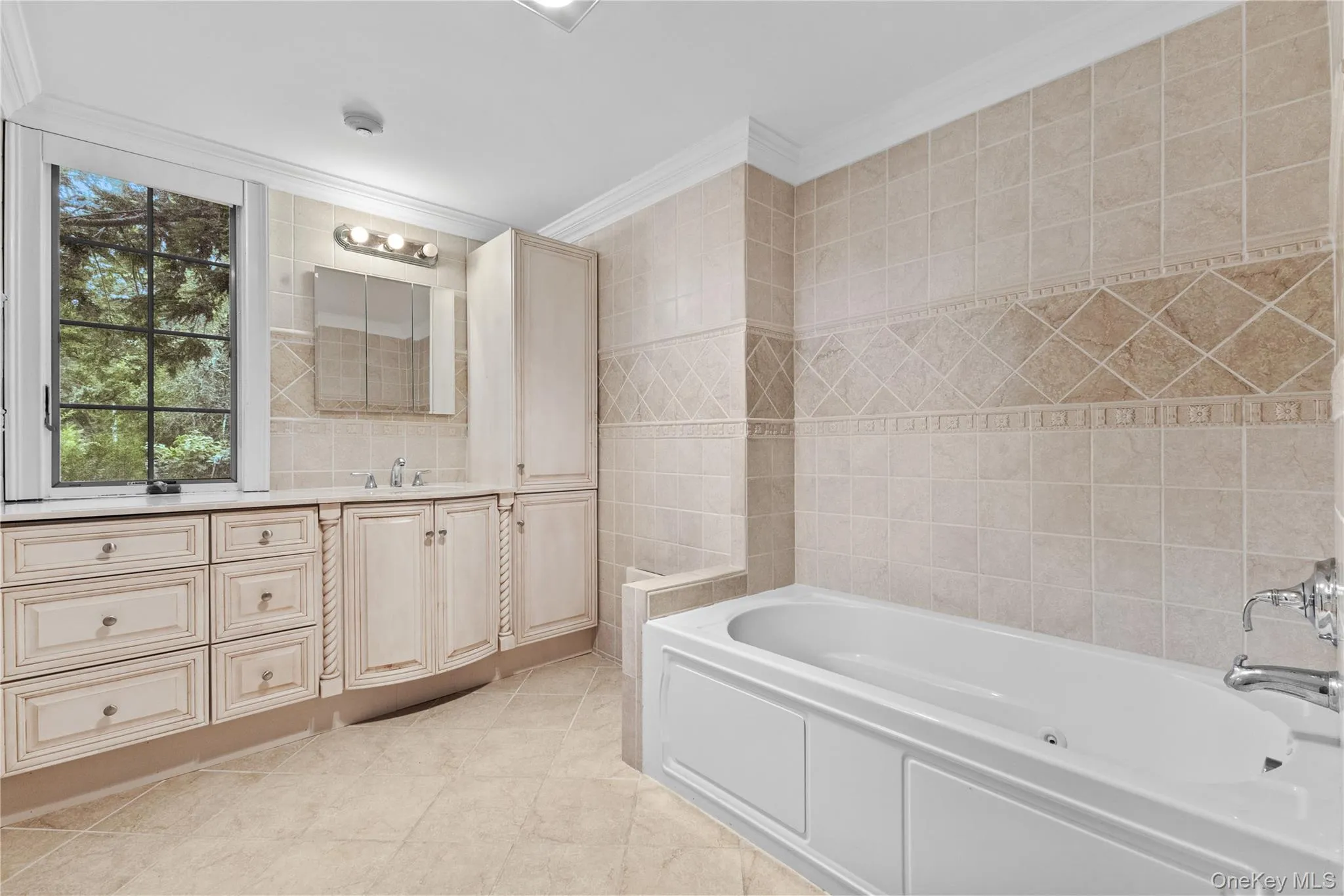 Full bathroom with tile walls, a garden tub, vanity, ornamental molding, and light tile patterned flooring Full bathroom with tile walls, a garden tub, vanity, ornamental molding, and light tile patterned flooring
