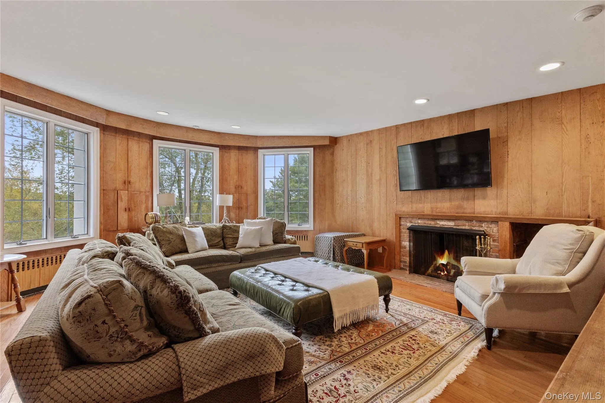 Living room with wooden walls, wood finished floors, a warm lit fireplace, radiator, and recessed lighting Living room with wooden walls, wood finished floors, a warm lit fireplace, radiator, and recessed lighting