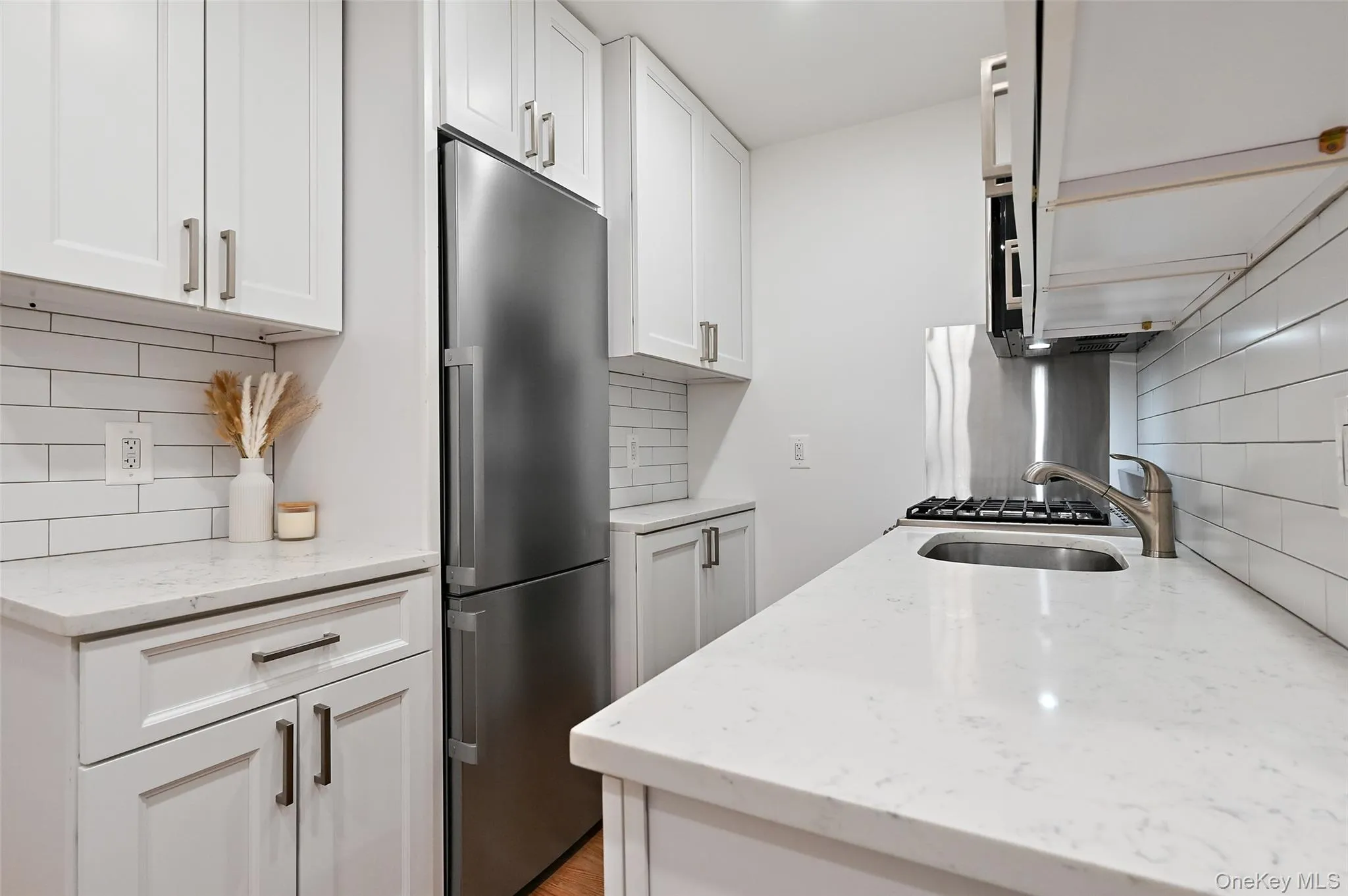 Kitchen featuring light stone counters, stainless steel appliances, backsplash, and white cabinetry Kitchen featuring light stone counters, stainless steel appliances, backsplash, and white cabinetry