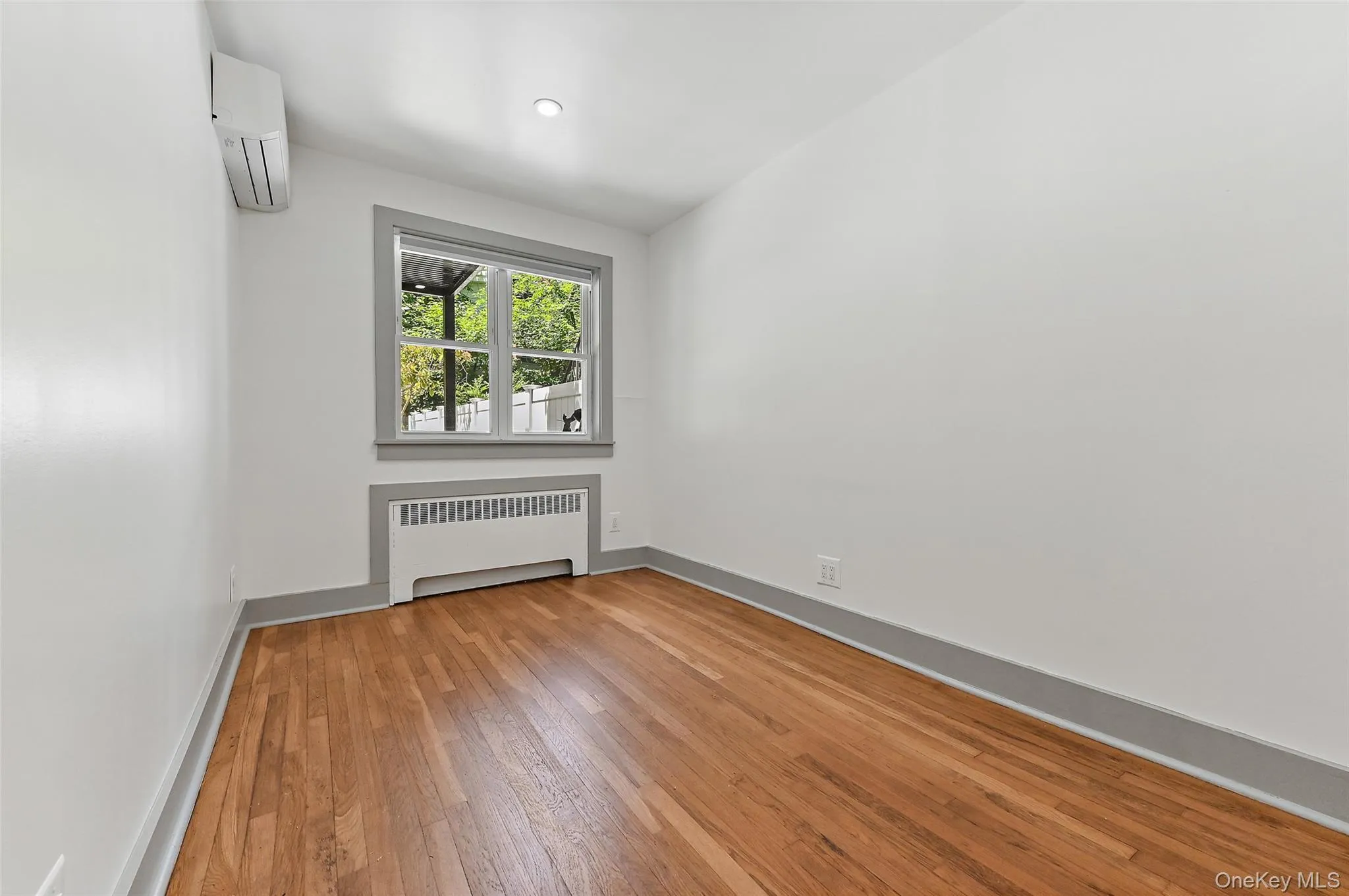 Unfurnished room with radiator, light wood-style floors, and a wall mounted air conditioner Unfurnished room with radiator, light wood-style floors, and a wall mounted air conditioner
