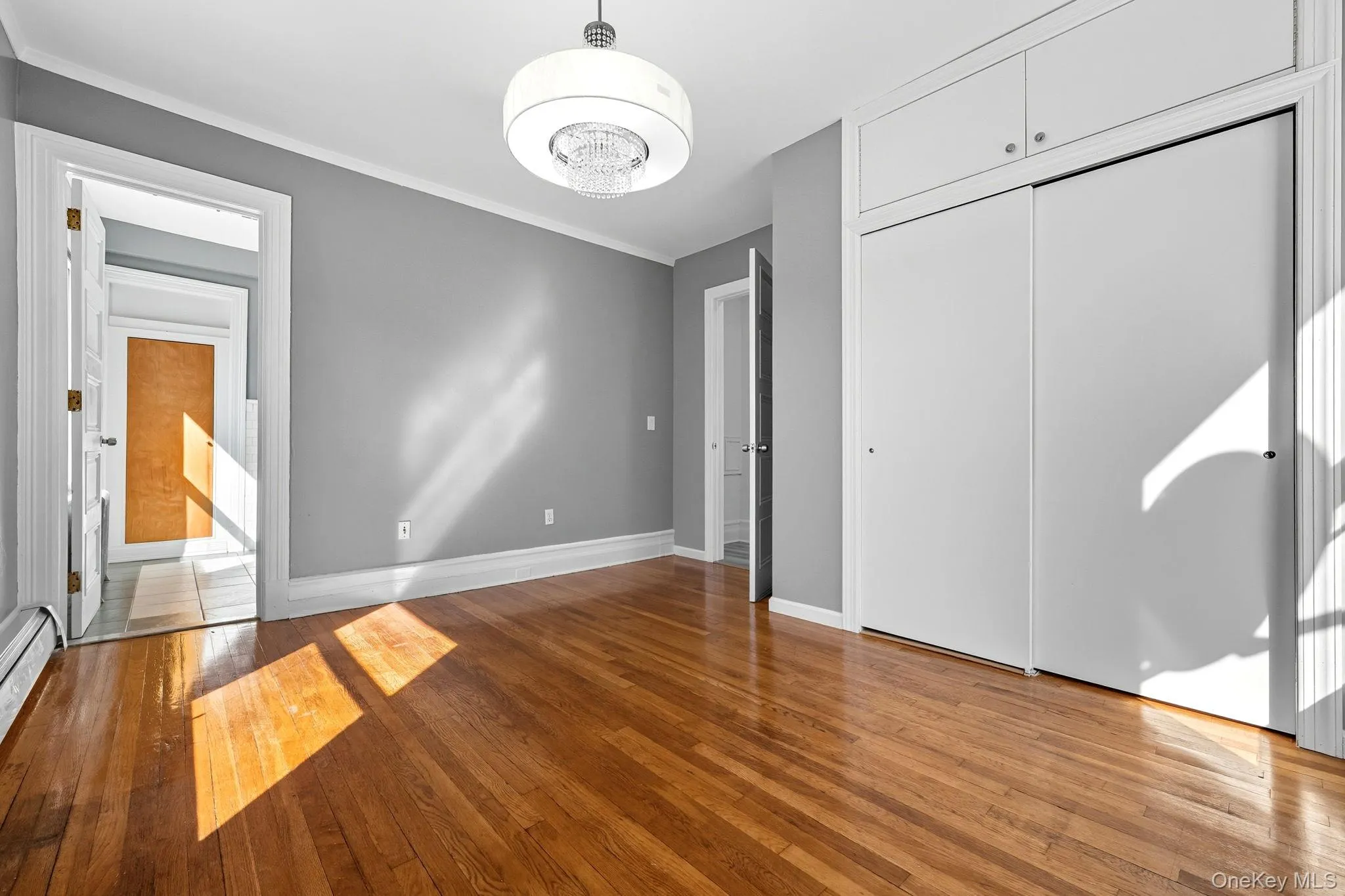 Unfurnished bedroom featuring light wood-type flooring, ornamental molding, a closet, and a baseboard heating unit Unfurnished bedroom featuring light wood-type flooring, ornamental molding, a closet, and a baseboard heating unit