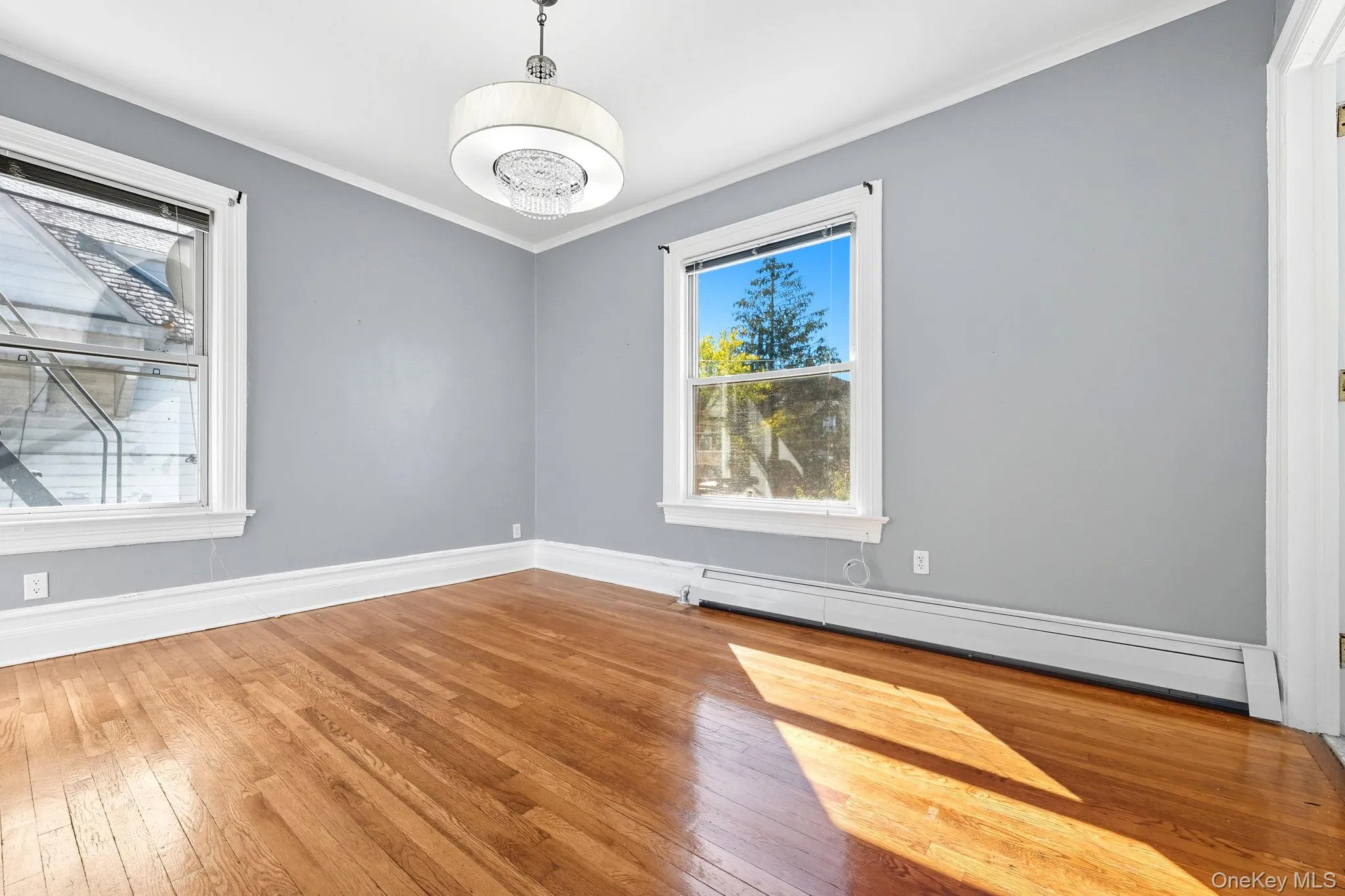 Unfurnished room featuring crown molding, baseboard heating, and wood-type flooring Unfurnished room featuring crown molding, baseboard heating, and wood-type flooring
