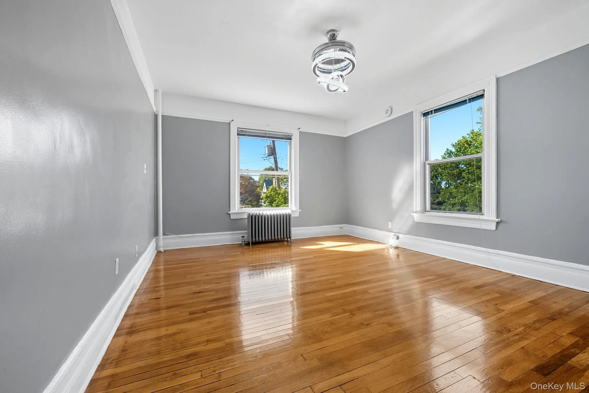 Unfurnished room featuring plenty of natural light, hardwood / wood-style floors, and radiator Unfurnished room featuring plenty of natural light, hardwood / wood-style floors, and radiator