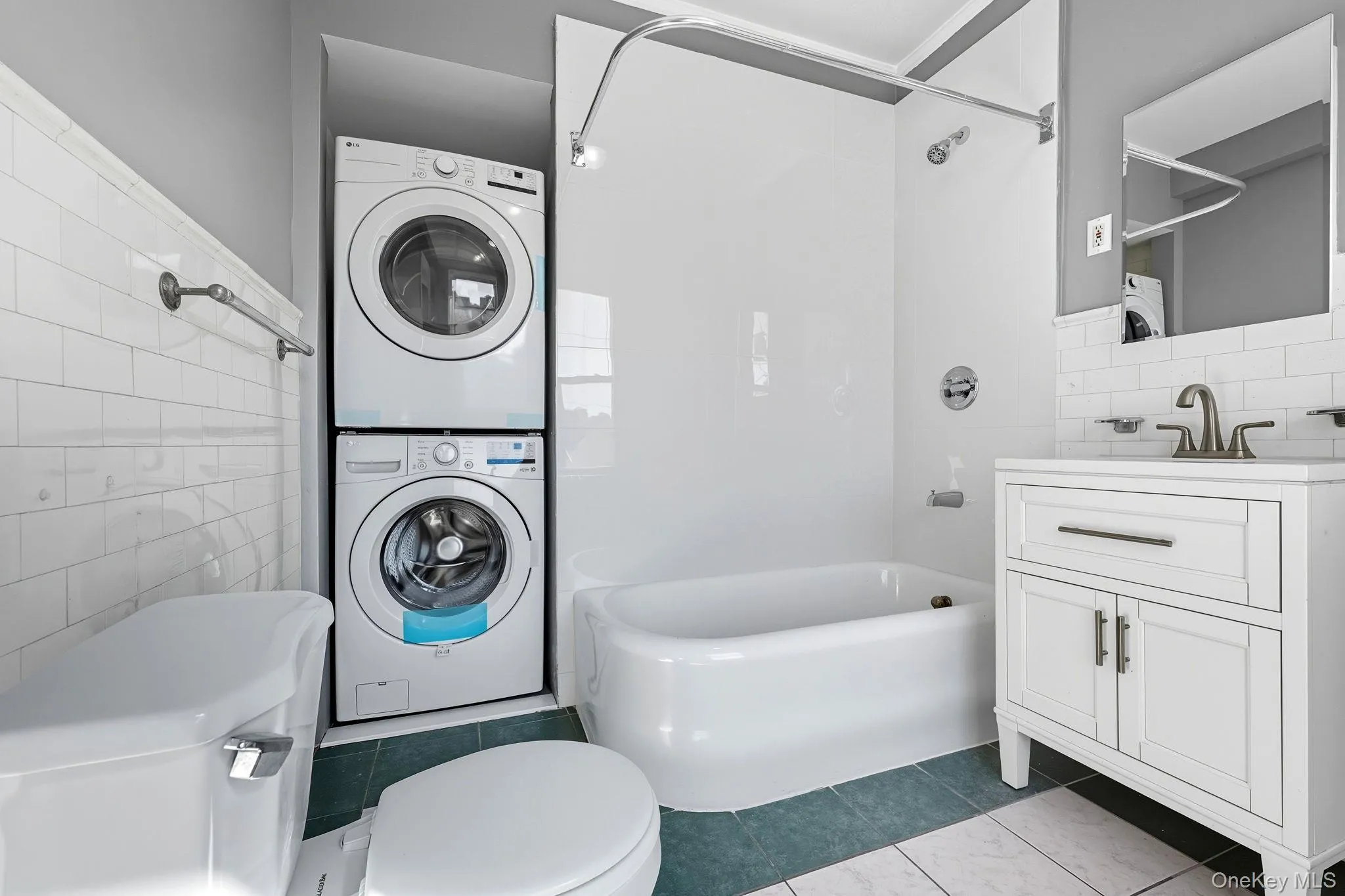 Full bath with tile walls, shower / washtub combination, tile patterned flooring, vanity, and stacked washing machine and dryer Full bath with tile walls, shower / washtub combination, tile patterned flooring, vanity, and stacked washing machine and dryer