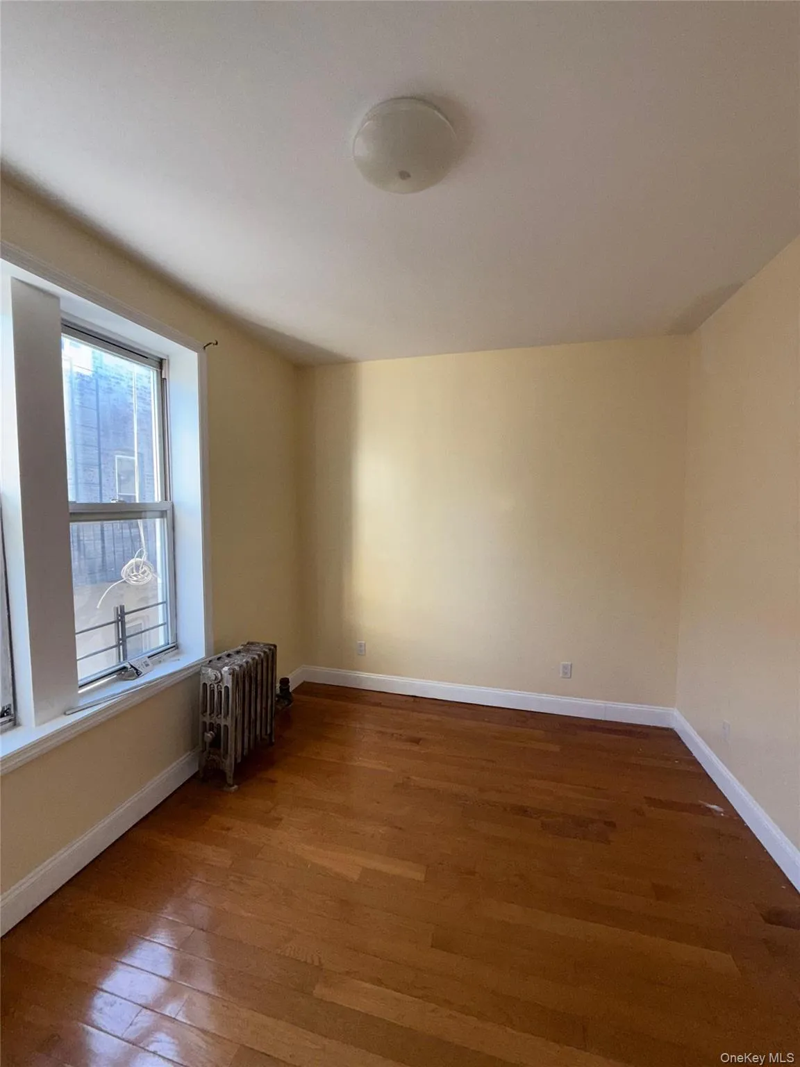 Unfurnished room featuring radiator and wood finished floors Unfurnished room featuring radiator and wood finished floors
