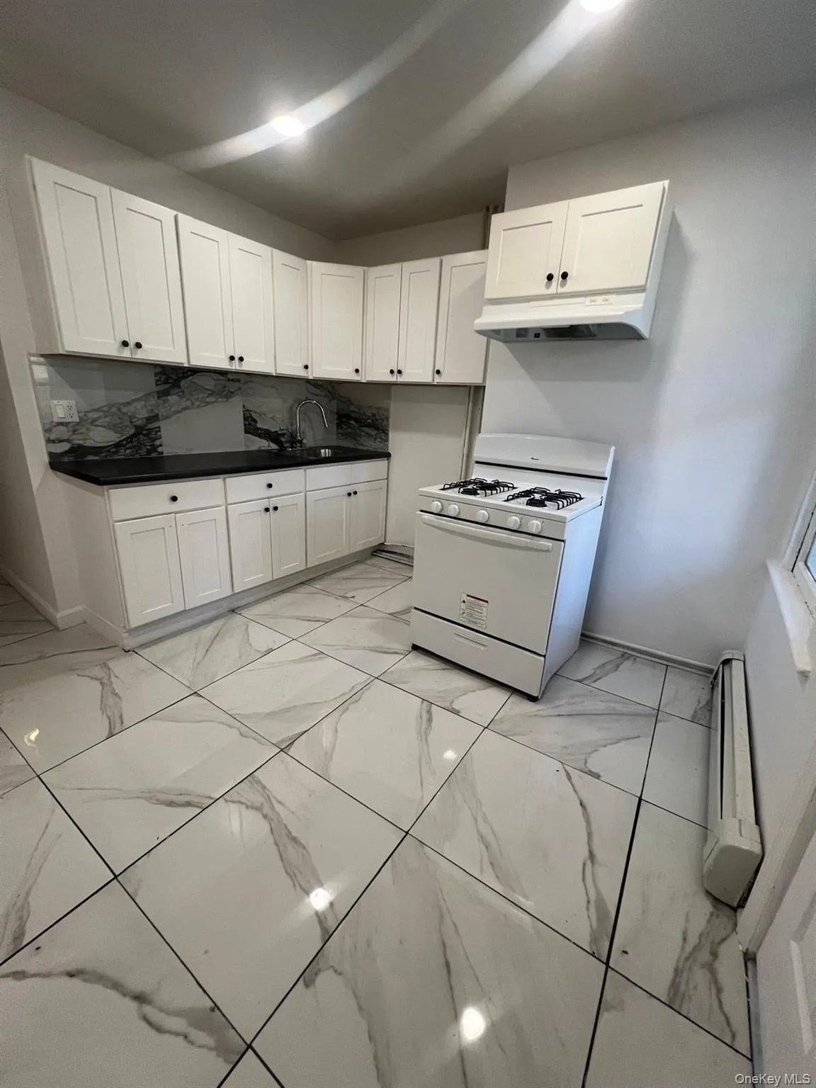 Kitchen with gas range gas stove, white cabinetry, light marble finish floors, dark countertops, and under cabinet range hood Kitchen with gas range gas stove, white cabinetry, light marble finish floors, dark countertops, and under cabinet range hood