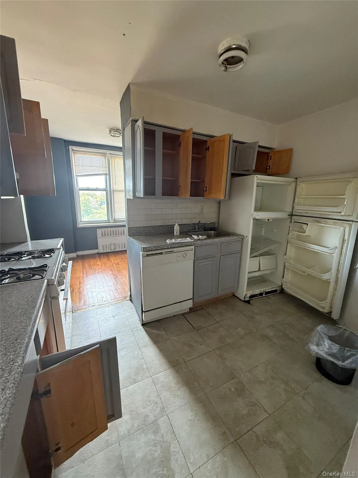 Kitchen featuring white appliances, radiator heating unit, tasteful backsplash, brown cabinetry, and light tile patterned flooring Kitchen featuring white appliances, radiator heating unit, tasteful backsplash, brown cabinetry, and light tile patterned flooring
