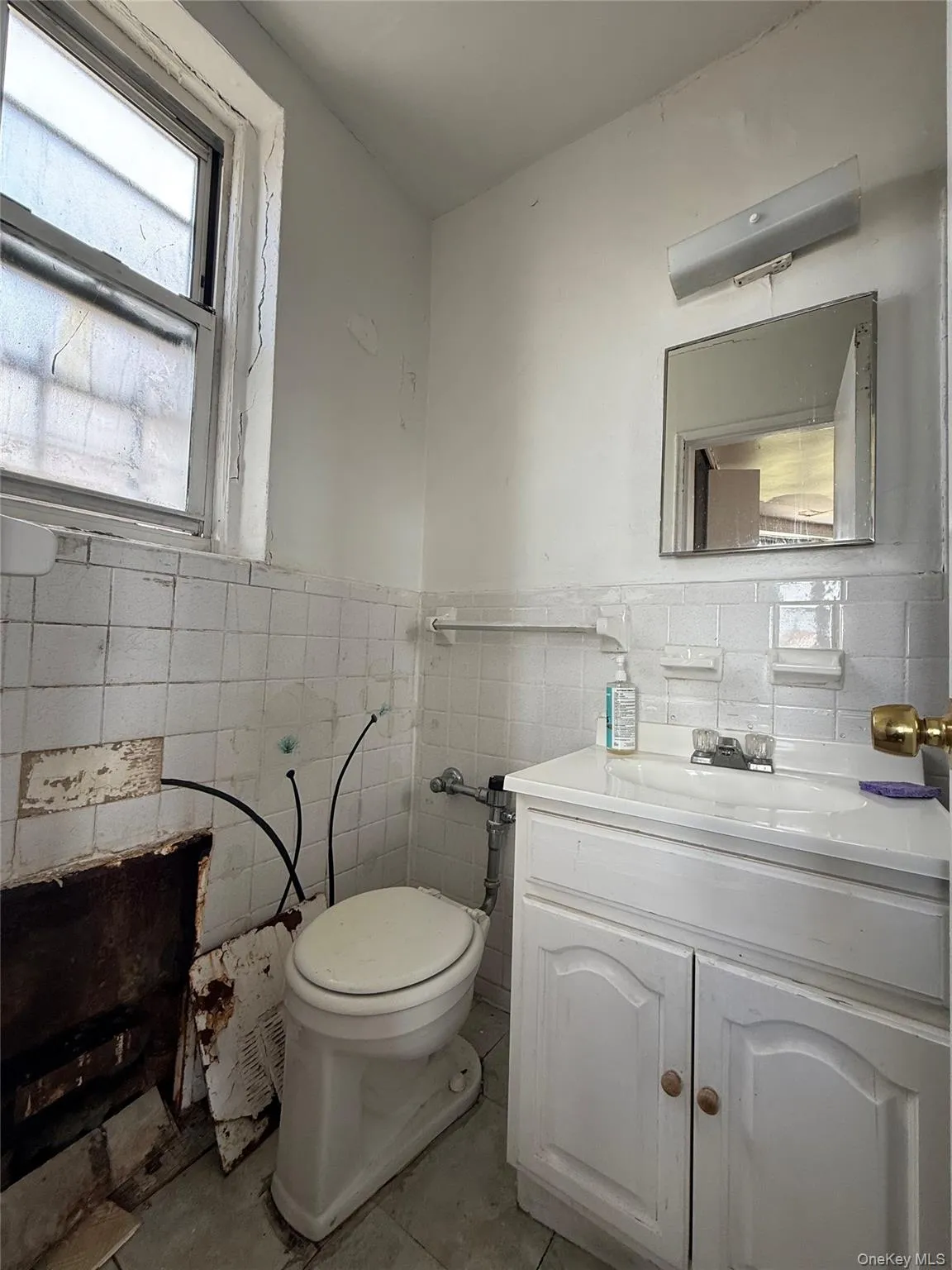 Half bath with vanity, tile walls, a wainscoted wall, and light tile patterned floors Half bath with vanity, tile walls, a wainscoted wall, and light tile patterned floors