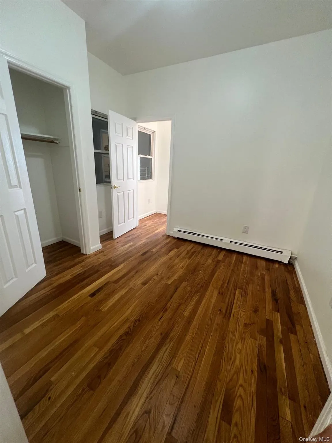 Unfurnished bedroom with dark wood-type flooring, a baseboard radiator, and a closet Unfurnished bedroom with dark wood-type flooring, a baseboard radiator, and a closet