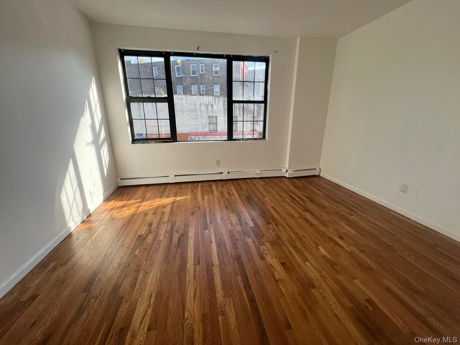 Unfurnished room with dark wood-style flooring and a baseboard radiator Unfurnished room with dark wood-style flooring and a baseboard radiator