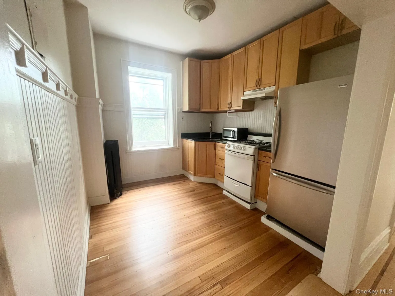 Kitchen featuring appliances with stainless steel finishes, dark countertops, light wood-type flooring, under cabinet range hood, and light brown cabinetry Kitchen featuring appliances with stainless steel finishes, dark countertops, light wood-type flooring, under cabinet range hood, and light brown cabinetry